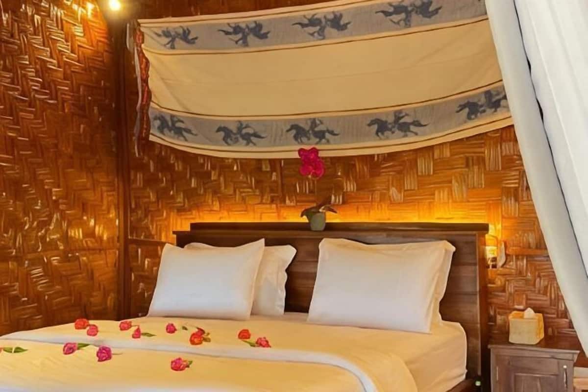 A bed with white bedding and a canopy, a wooden headboard, and a nightstand with a lamp.