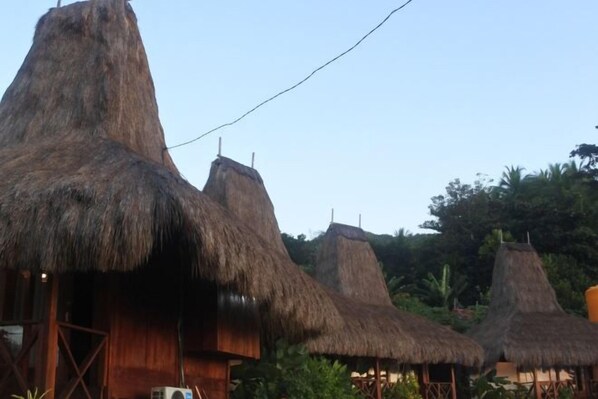 Thatched-roof huts with wooden structures, likely part of a resort or accommodation area. - Three Queen Villa and Homestay (Wanokaka)