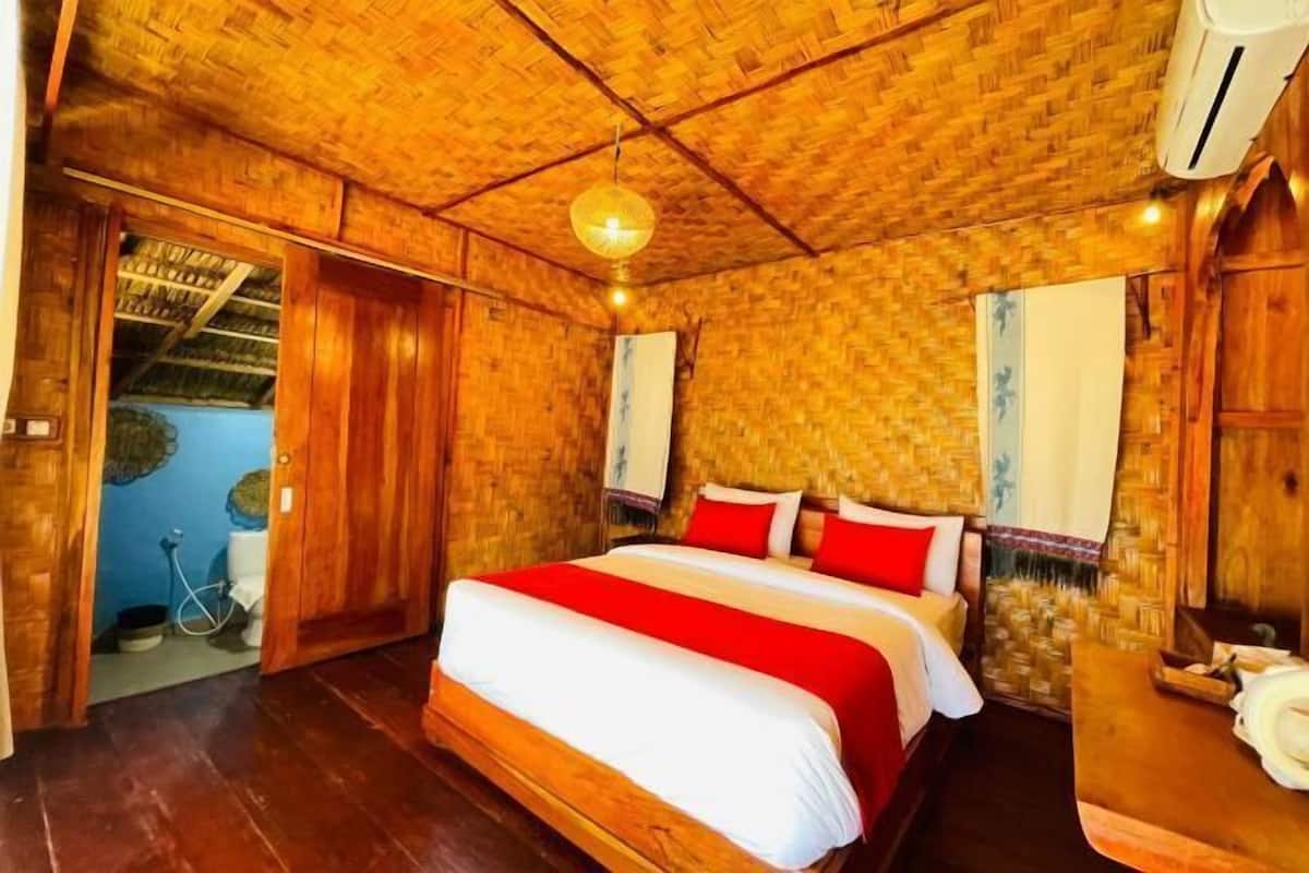 A wooden room with a bed, a hanging light fixture, and a door leading to another room.
