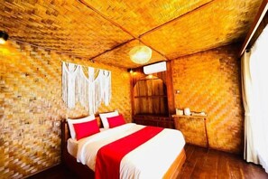 A room with a woven ceiling, a bed with red and white bedding, a wooden wardrobe, and a hanging light fixture.