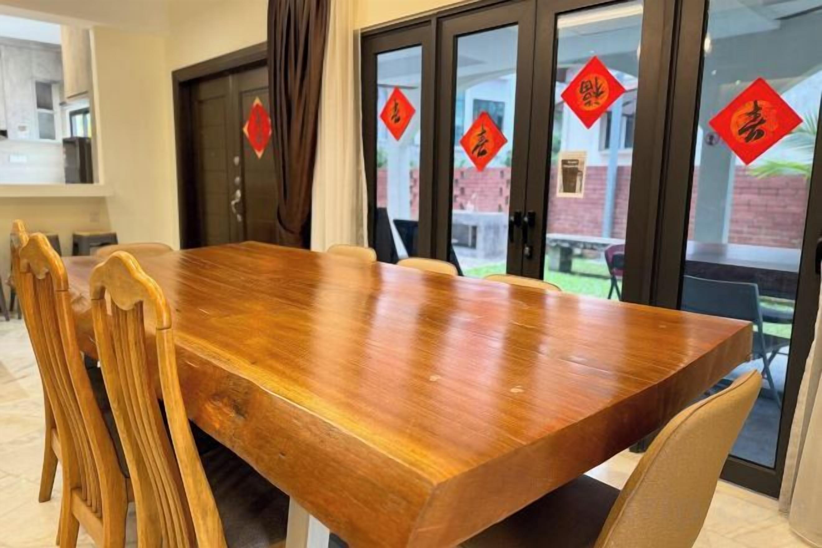 Una mesa de madera con sillas, una zona de cocina y vistas a través de puertas de cristal con adornos rojos.