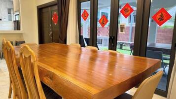 Una mesa de madera con sillas, una zona de cocina y vistas a través de puertas de cristal con adornos rojos.