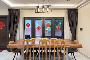 A dining area with a wooden table and chairs, a chandelier, and curtains. - Gathering l Wedding House l 18PaxTaman Oug KL (Kuala Lumpur)
