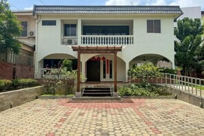 Un edificio de dos plantas con una entrada central, un balcón y un patio empedrado.
