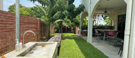 Une terrasse avec un évier en pierre, une pelouse et un espace détente avec des chaises et une table.