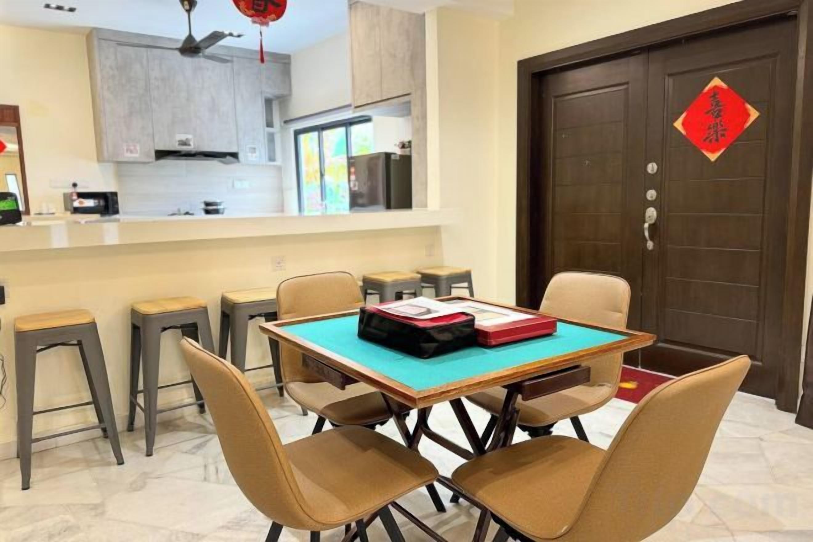 A dining area with a table and chairs, a kitchen in the background, and a traditional door with a red decoration.