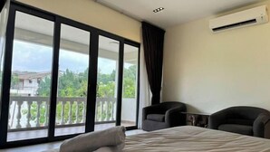 A hotel room with a bed, two chairs, a small table, and a balcony with a view of greenery and buildings. - Gathering l Wedding House l 18PaxTaman Oug KL (Kuala Lumpur)