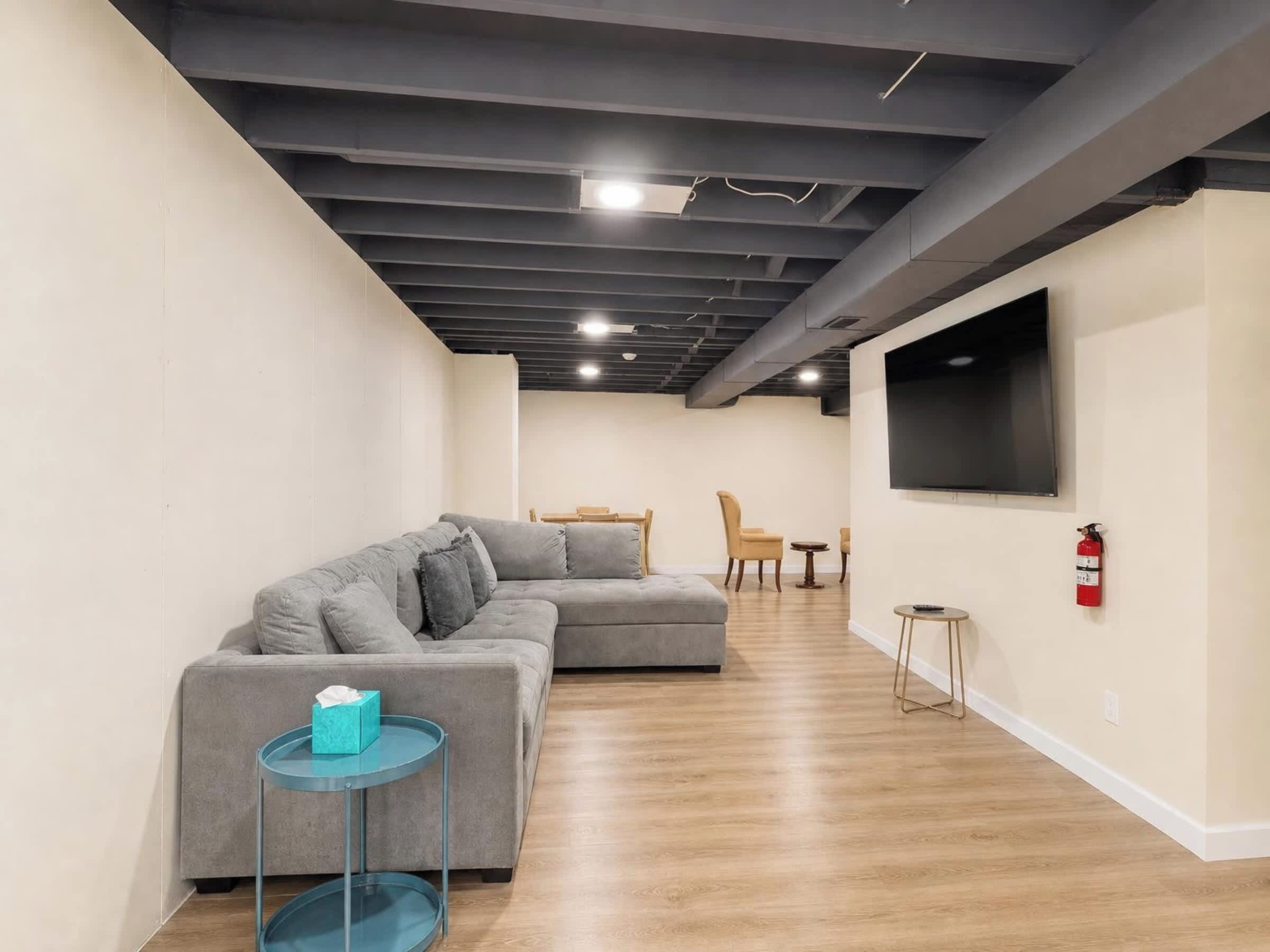 A modern living room with a sectional sofa, a small round table, and a flat-screen TV mounted on the wall.