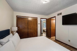 Una habitación de hotel con una cama, un armario de madera y un televisor montado en la pared.