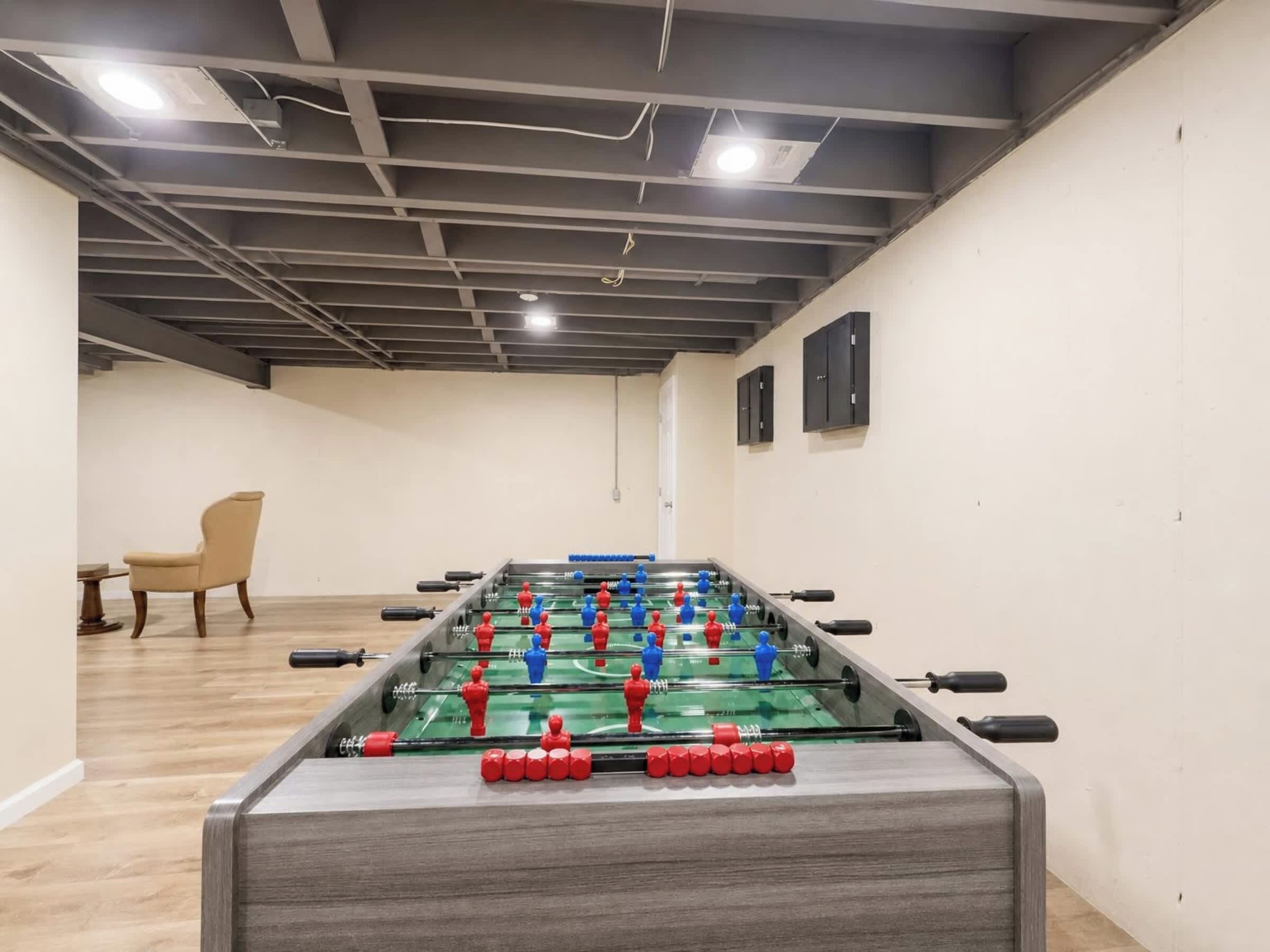 Una habitación con mesa de futbolín, una silla y una mesa con una botella.