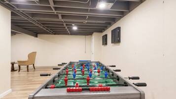 Una habitación con mesa de futbolín, una silla y una mesa con una botella.