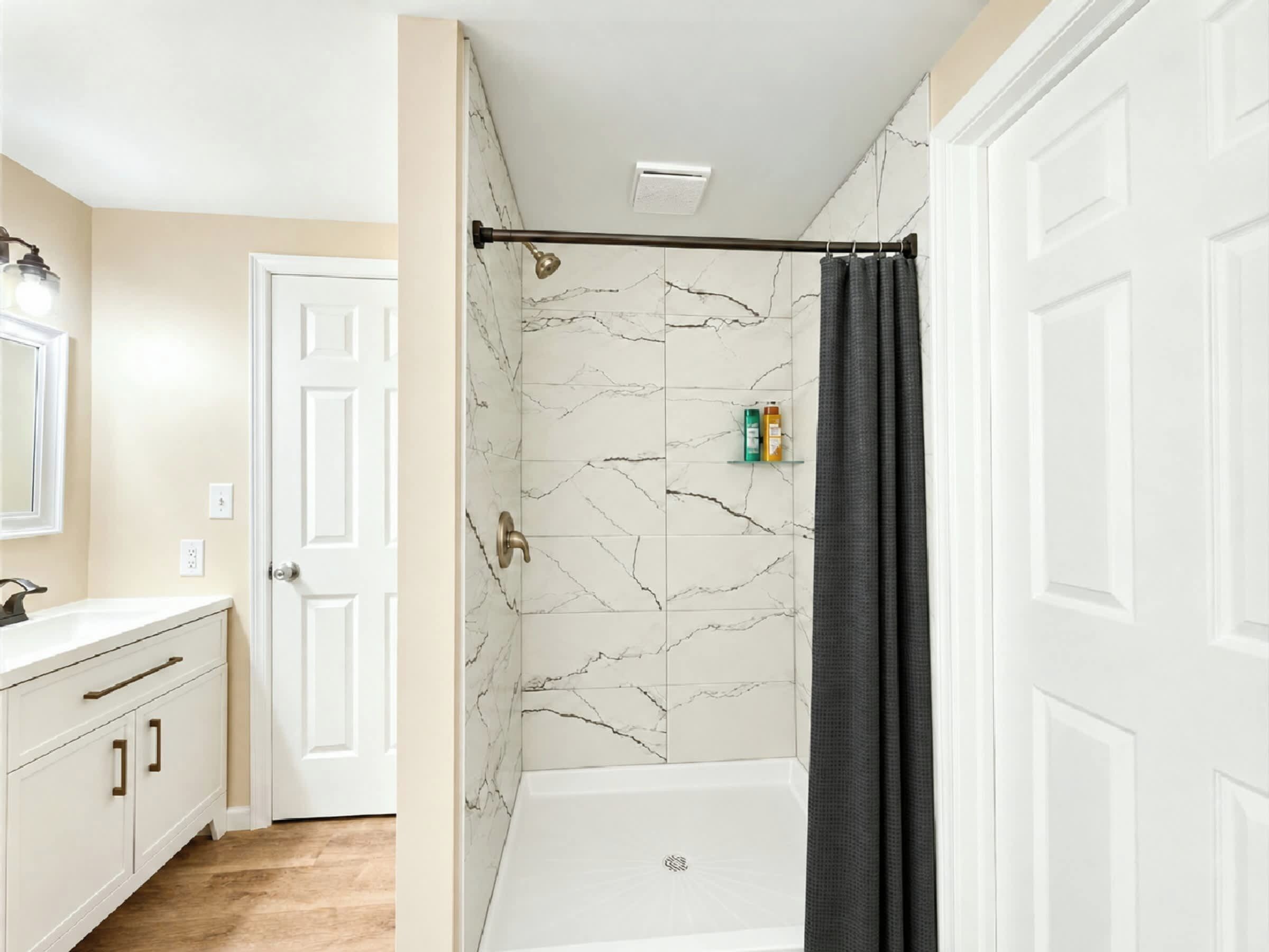 A bathroom with a white bathtub, marble wall tiles, a shower curtain, and a white door.