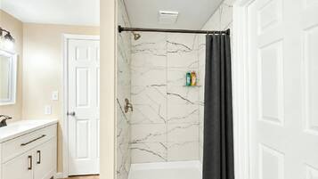 A bathroom with a white bathtub, marble wall tiles, a shower curtain, and a white door.