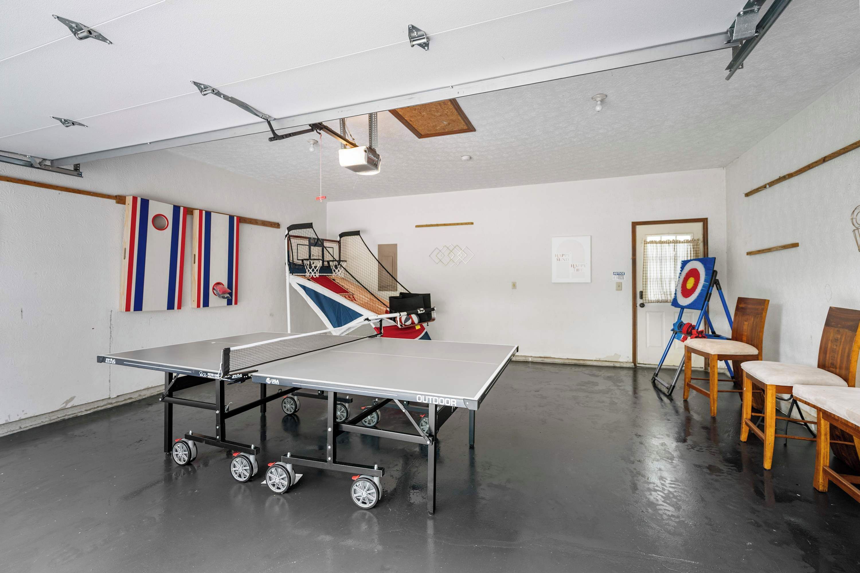 Una mesa de ping pong con un carrito, un objetivo y sillas en una habitación con paredes blancas y suelo de madera.