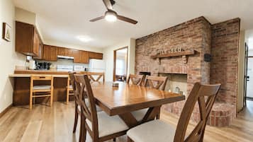 Un comedor con mesa y sillas de madera, ventilador de techo y chimenea de ladrillo.