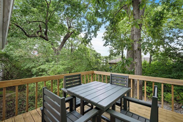 A wooden deck with a table and chairs, surrounded by trees and greenery. - The Family Nook - Home for 8 (Hamilton)