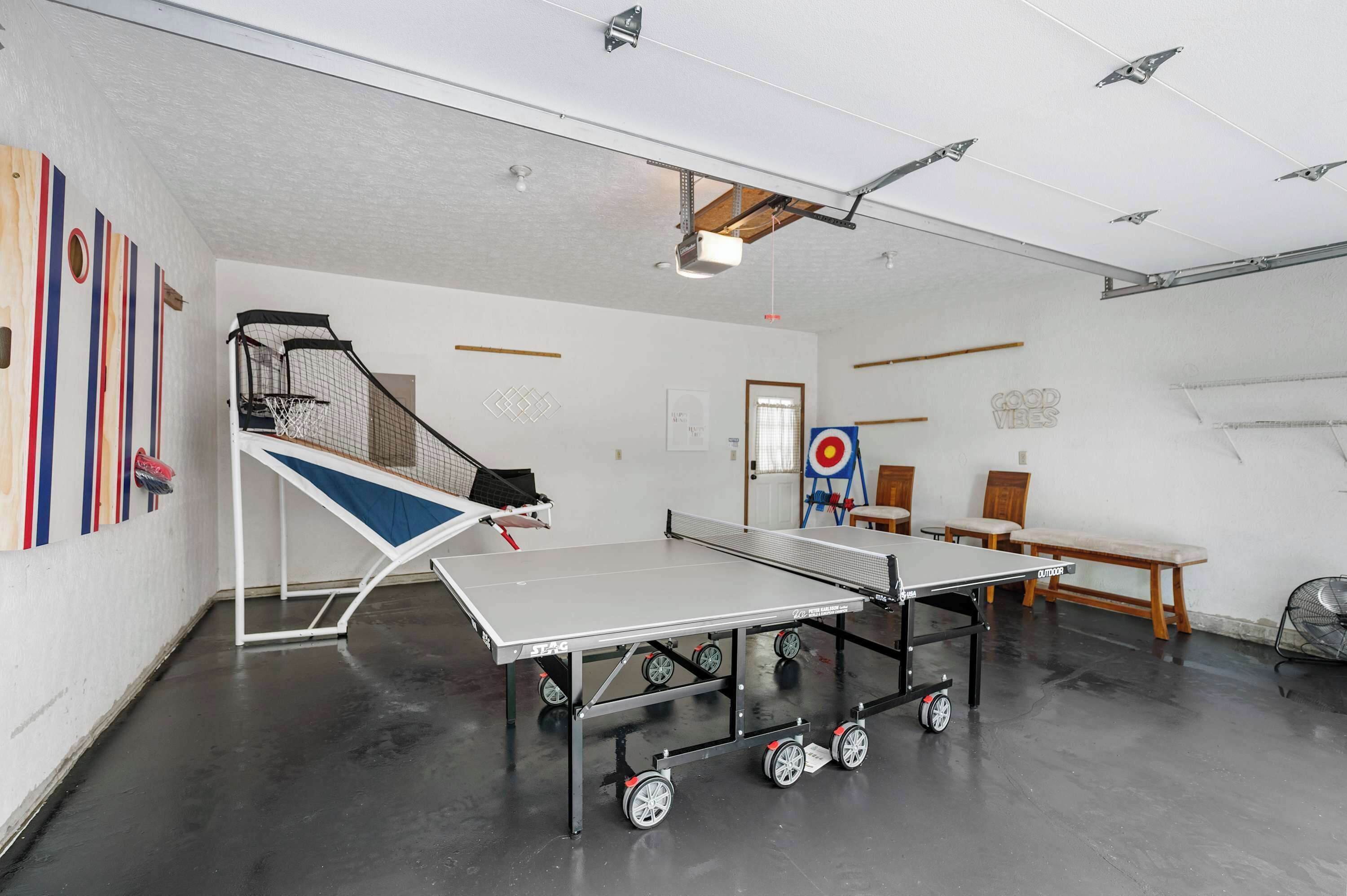 A spacious room with a ping pong table, a small basketball hoop, and a target on the wall.