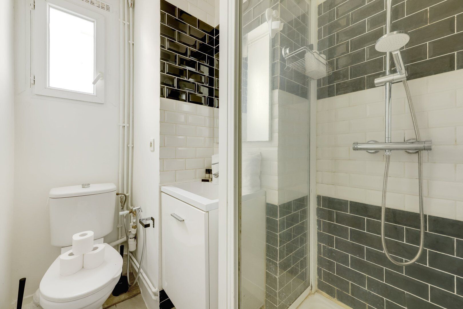 Un baño con inodoro, ducha con puerta de cristal y pared de azulejos.