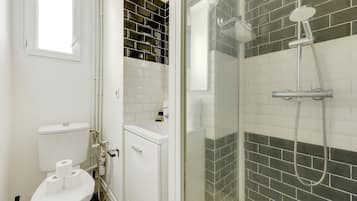 Un baño con inodoro, ducha con puerta de cristal y pared de azulejos.