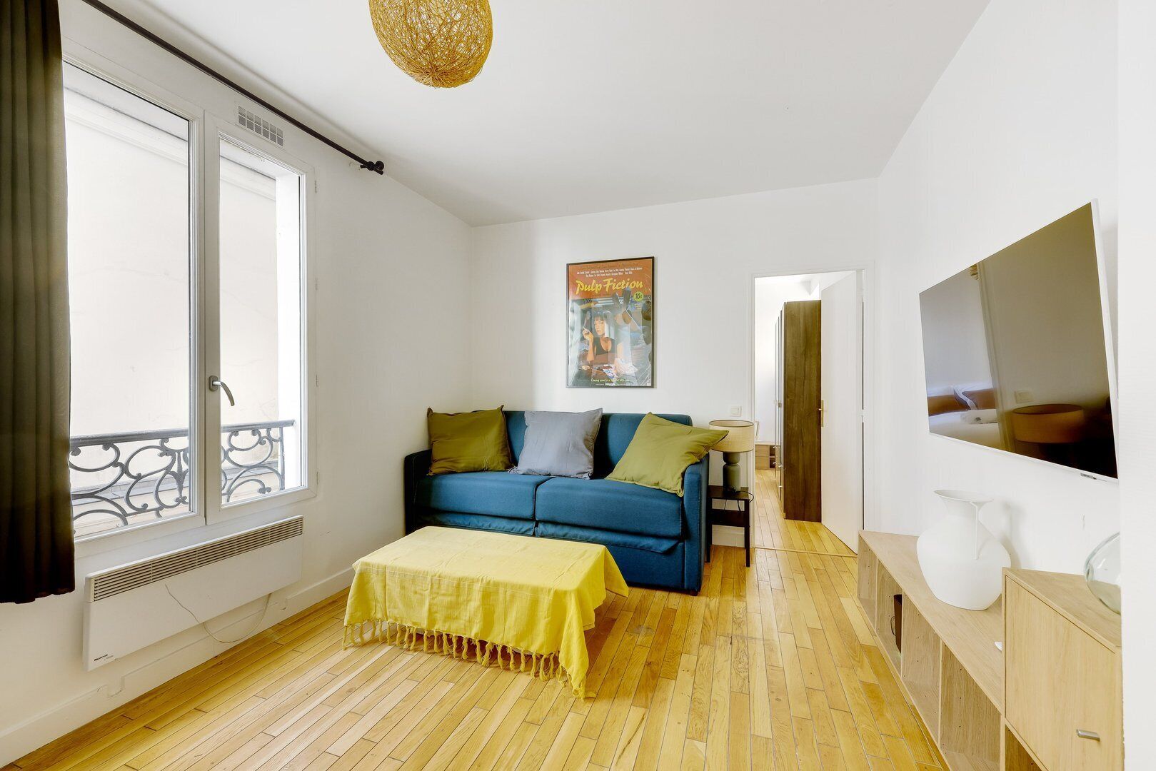 Una sala de estar moderna con un sofá azul, una mesa amarilla y un televisor grande.