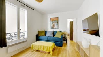 Una sala de estar moderna con un sofá azul, una mesa amarilla y un televisor grande.