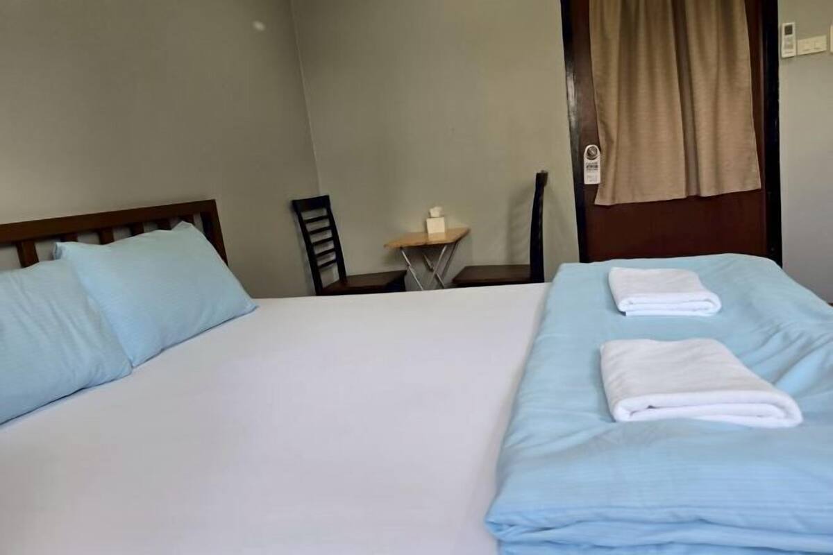 A hotel room with two beds, a small table with a tissue box, a chair, and a curtain.