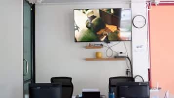 A room with a flat-screen TV mounted on the wall, two computer monitors on a desk, a clock, and a Wi-Fi sign.