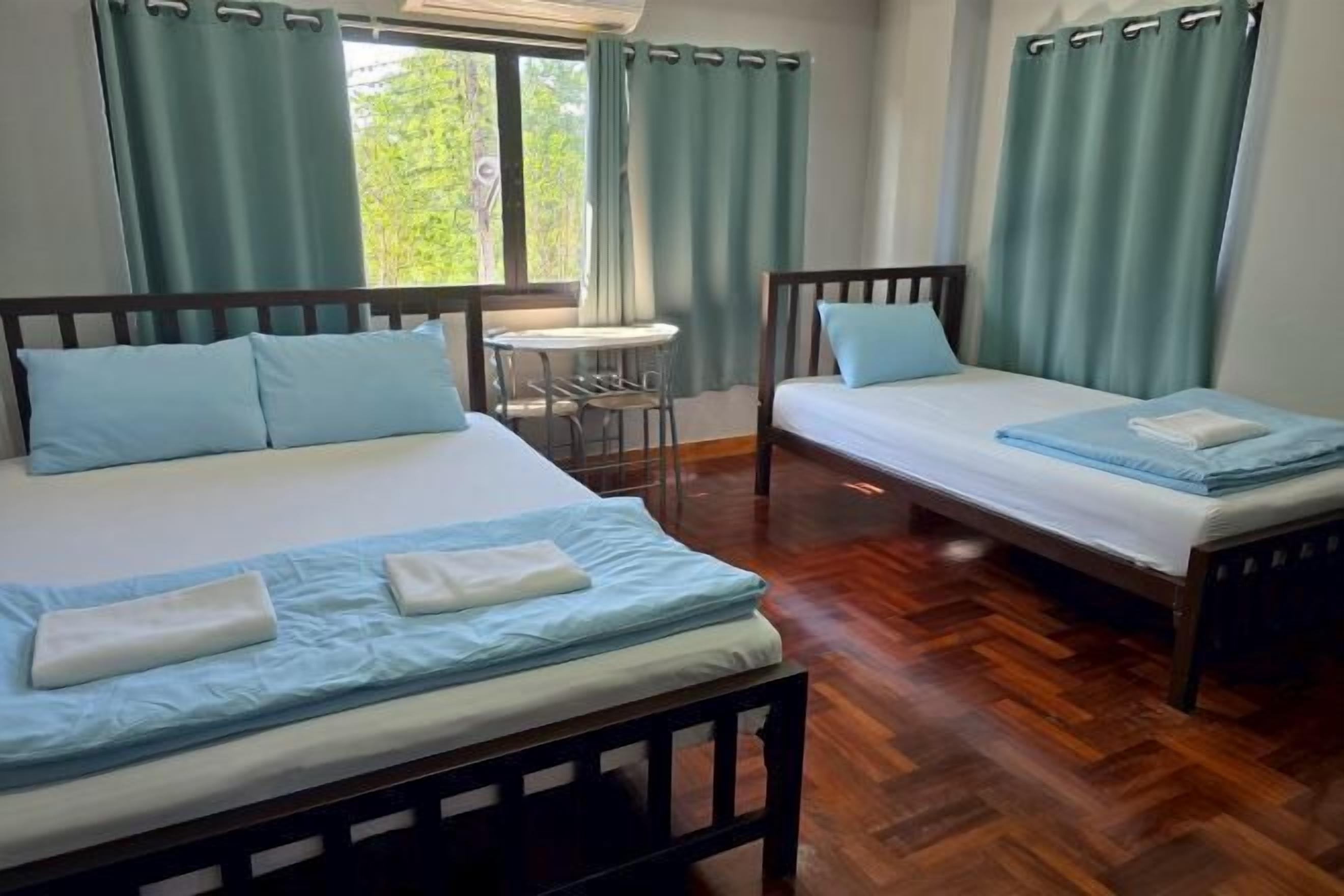 A room with two beds, a small table, and a window with curtains.