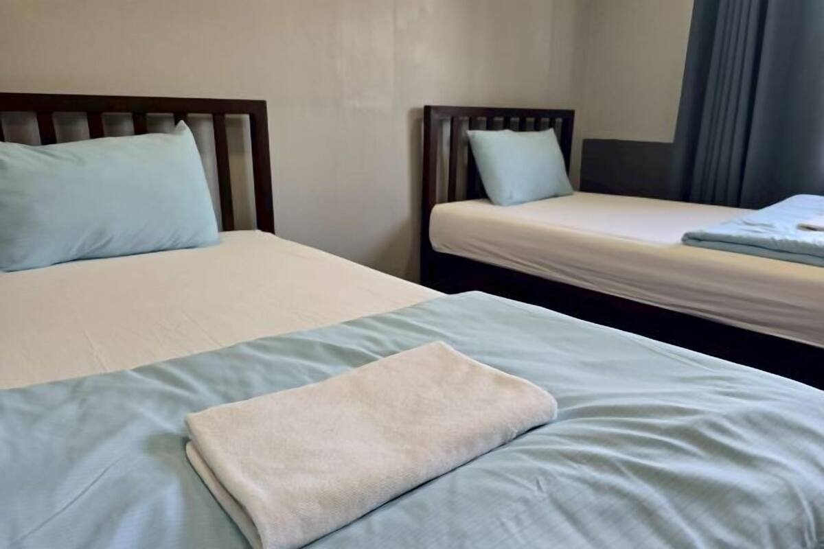 A hotel room with two beds, each with a pillow and a blanket.