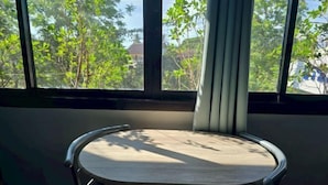 Una mesa redonda con superficie clara, ubicada cerca de una ventana que ofrece vistas a árboles y edificios.