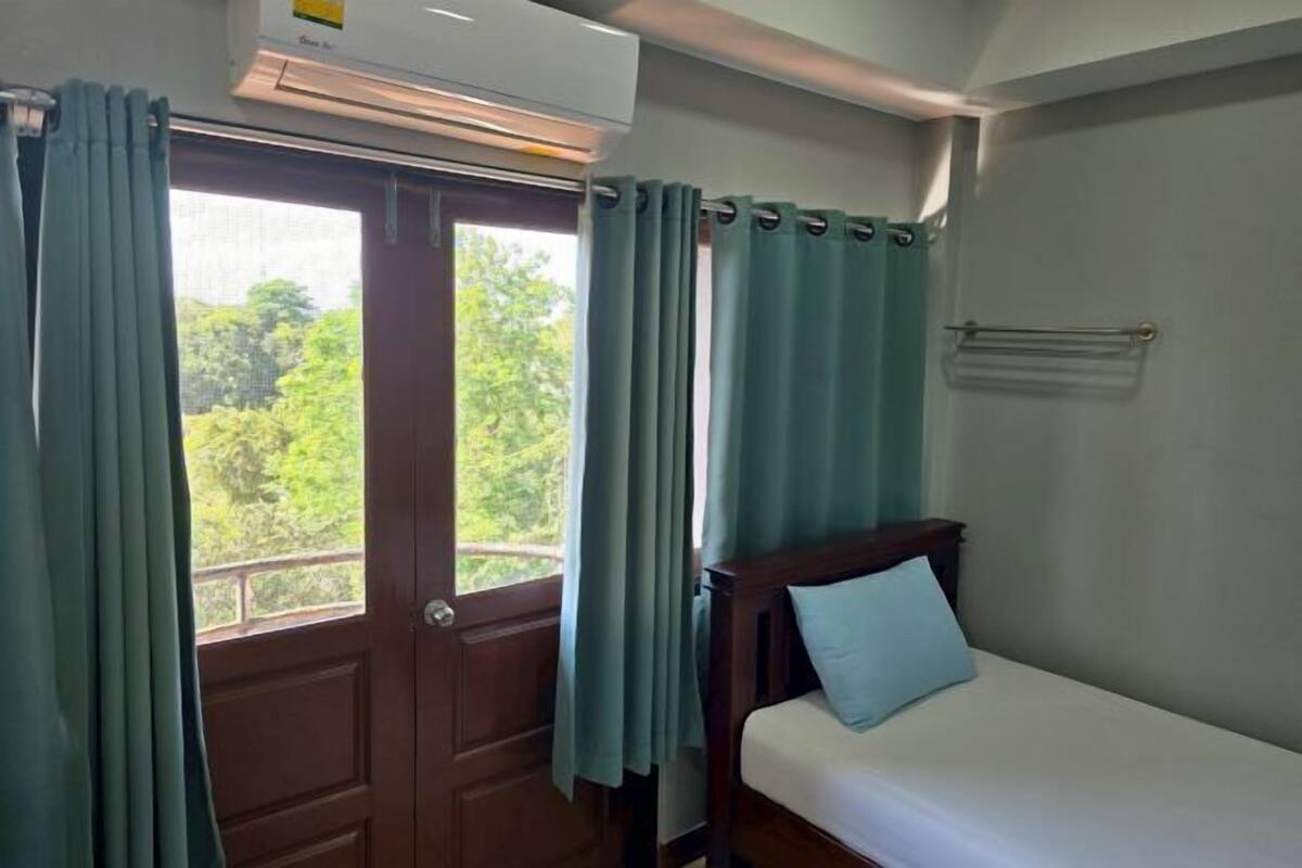 A room with a bed, a window with curtains, an air conditioning unit, and a towel rack.