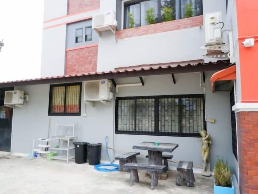 A building with a red and white facade, air conditioning units, a black-framed window, and a small outdoor seating area with a table and chairs.