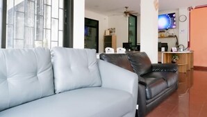 Un salón con un sofá gris y un sofá de cuero negro. Hay un televisor en la pared y una mesita con una planta.