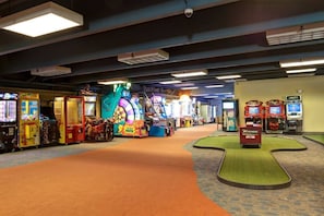 An indoor arcade with various gaming machines, a ticket booth, and a green carpeted area.