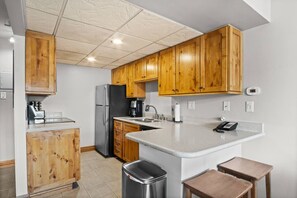 A kitchen with wooden cabinets, a stainless steel refrigerator, a coffee maker, and a trash can.