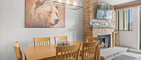A dining area with a wooden table and chairs, a bear painting on the wall, and a stone fireplace.