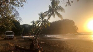 A beach scene with palm trees, a parked van, and a boat on the sand. - Resort style, ocean side, great location, WiFi, AC (Jacó)