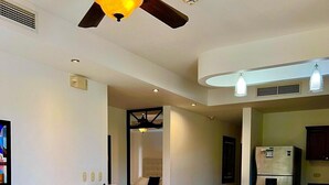 A modern living room with a white leather sofa, blue cushions, a glass coffee table, and a ceiling fan. - Resort style, ocean side, great location, WiFi, AC (Jacó)