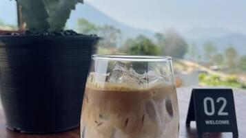 A glass of iced coffee on a table with a potted plant and a welcome sign.