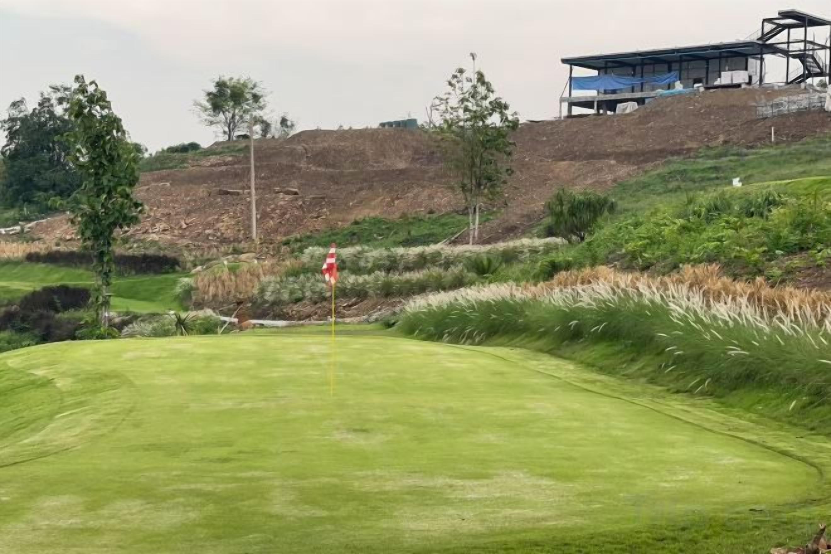 A golf course with a flagstick, bunkers, and a building in the background.