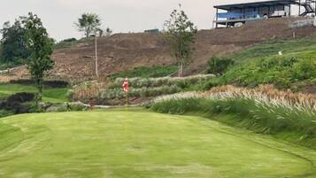 A golf course with a flagstick, bunkers, and a building in the background.