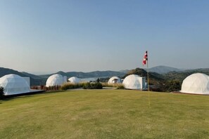 A grassy field with several dome-shaped structures, likely accommodations, and a flagpole with a flag.
