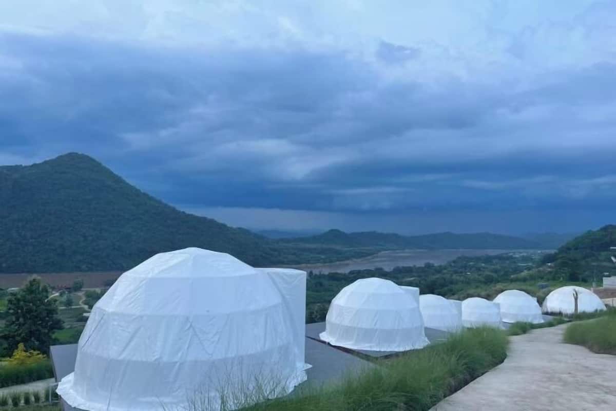 A row of white dome-shaped structures with a pathway leading to them, set against a backdrop of a mountainous landscape and cloudy sky.