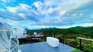Un espace extérieur moderne, aménagé pour se détendre, avec vue sur des collines verdoyantes et un ciel dégagé.