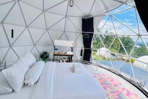 Ein Zeltraum mit Bett, Kissen, einem Ventilator und einem Tisch mit einer Wasserflasche.