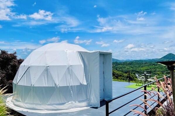 A dome-shaped tent-like structure with a roof, situated on a balcony with a view of a mountainous landscape.