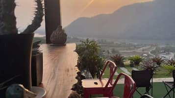 Una terraza con vistas a un valle y montañas, que incluye una mesa y sillas de madera.