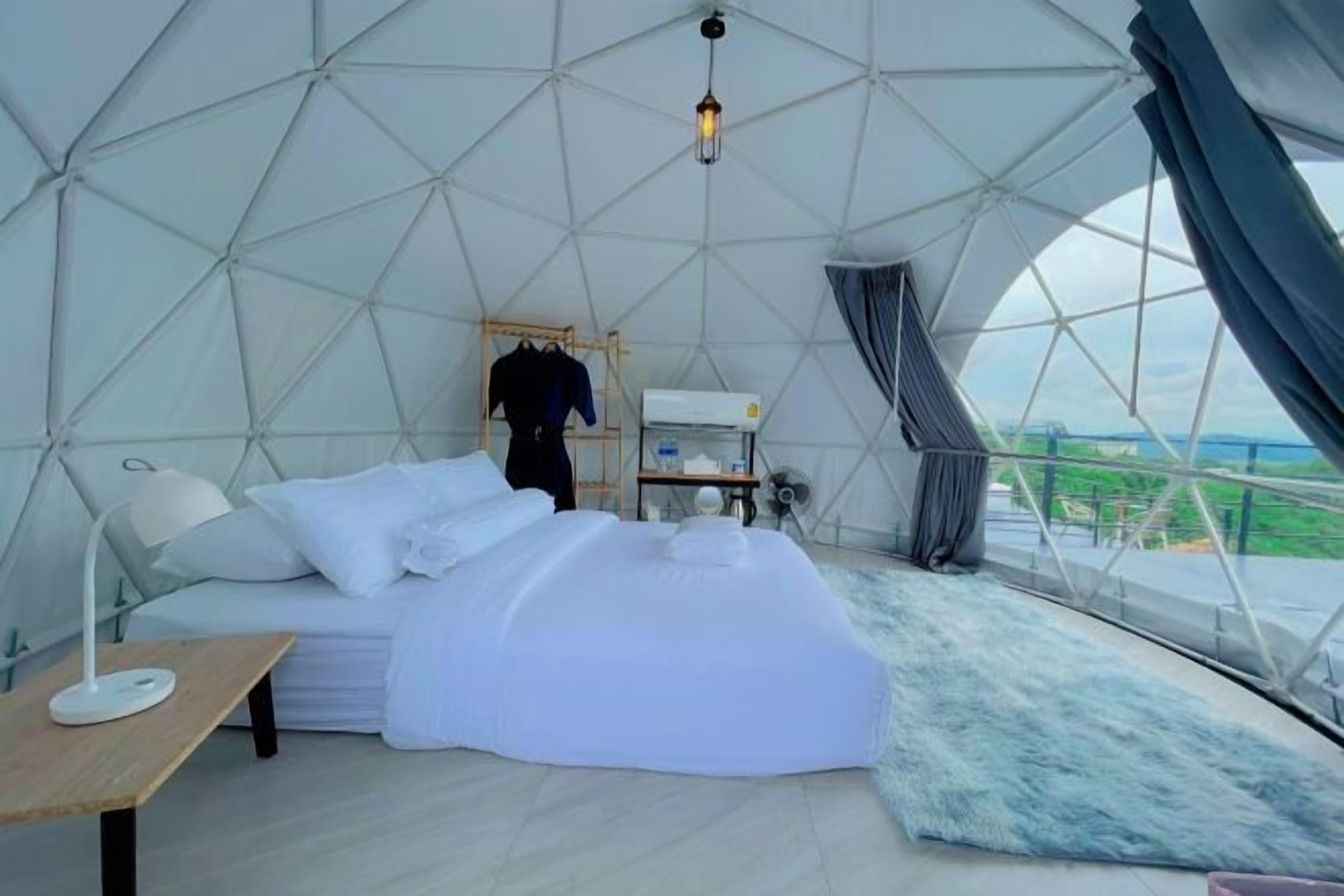 A dome-shaped room with a bed, a table, and a view through the dome's structure.