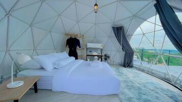 A dome-shaped room with a bed, a table, and a view through the dome's structure.