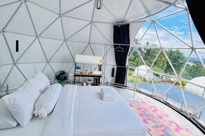 A tented accommodation with a bed, a fan, and a table with a lamp.